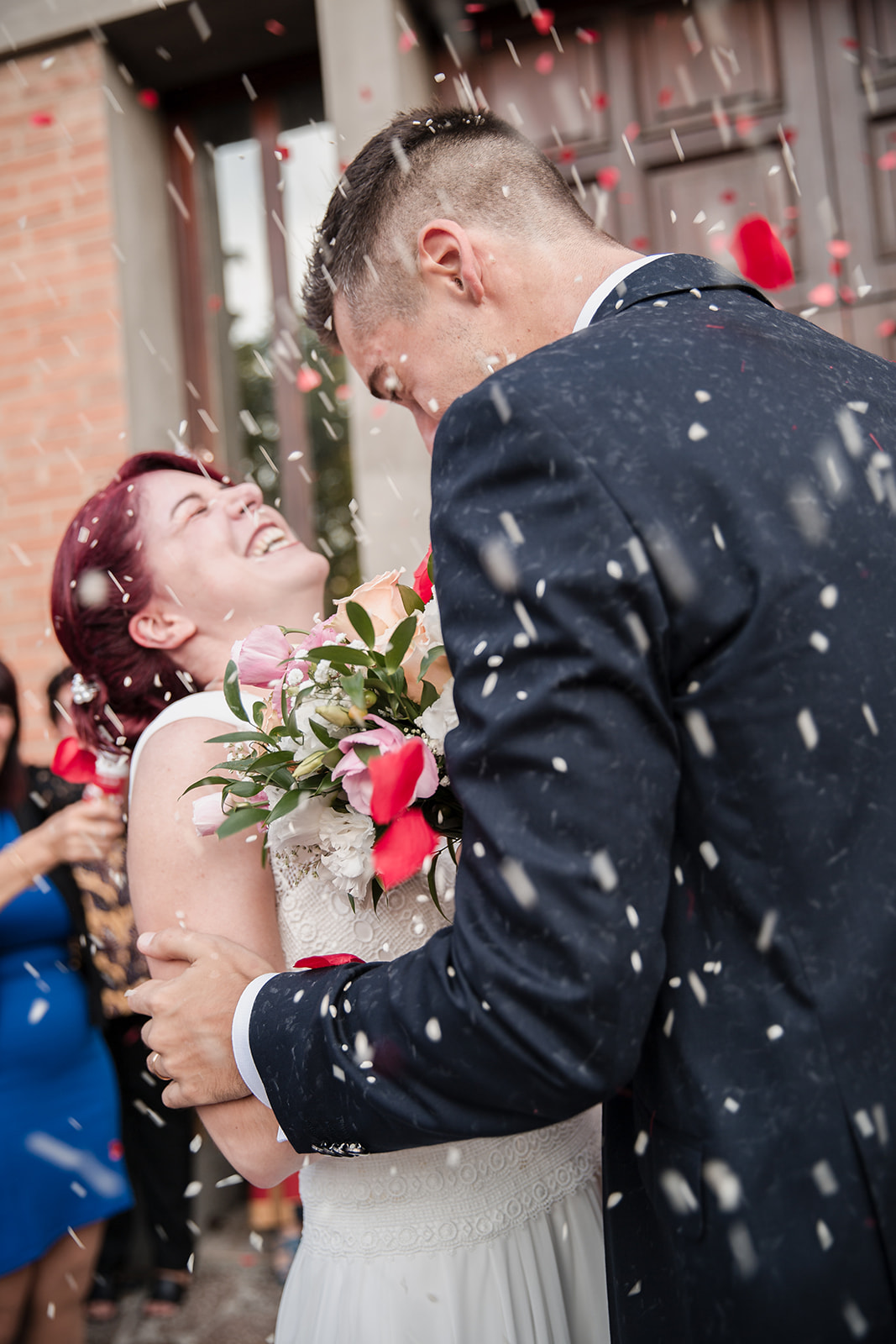 Anna and Lorenzo embracing as confetti is thrown after their wedding ceremony in Ferrara, Italy.